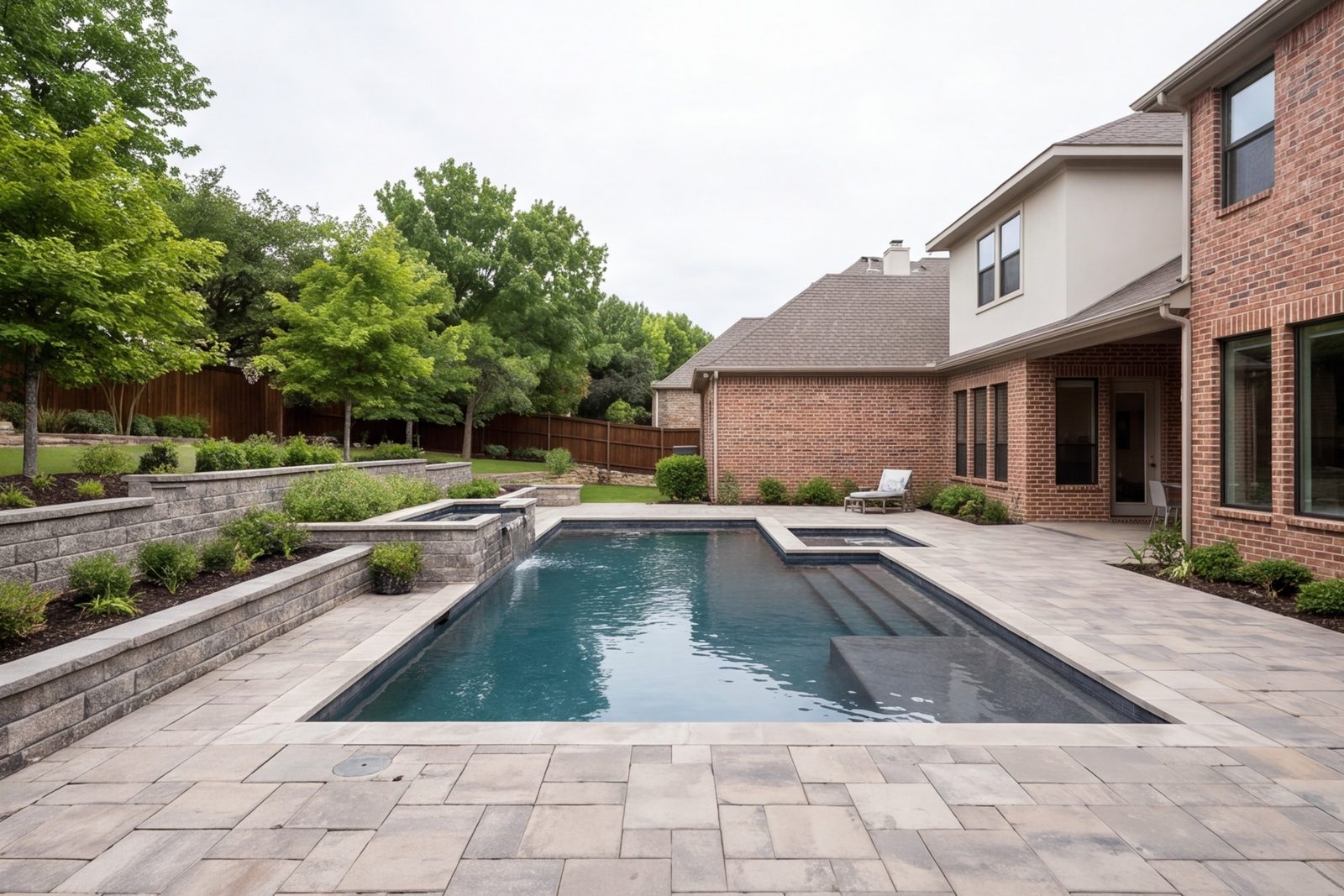 Back yard with a stone patio, retaining wall and pool deck connected to the house