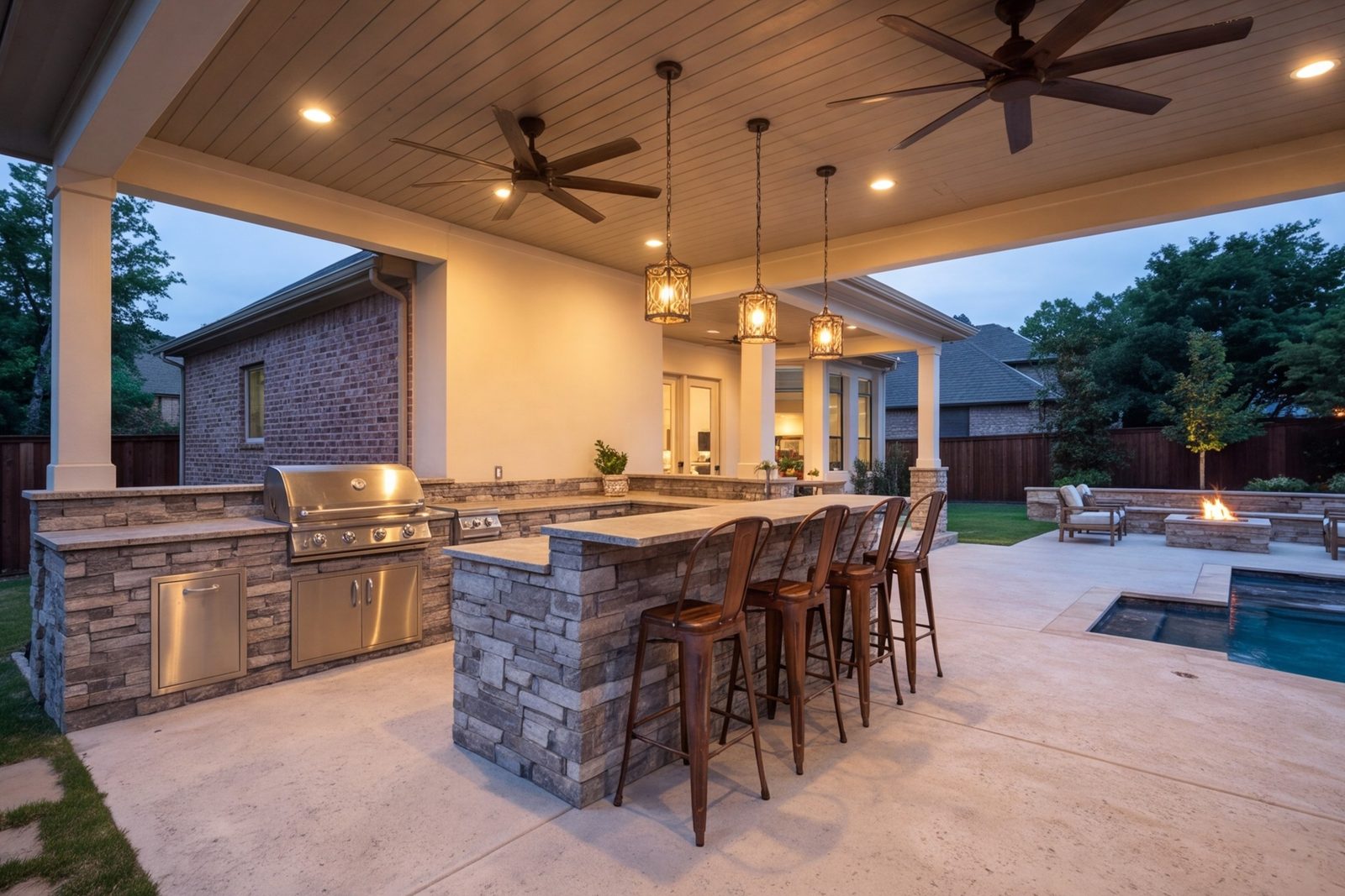 Covered patio with an outdoor kitchen, bar seating, ceiling fans and lighting at dusk